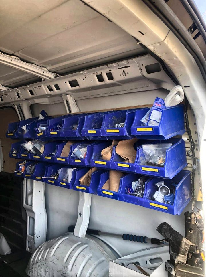 Three rows of labelled blue parts bins mounted along the wall of the service van