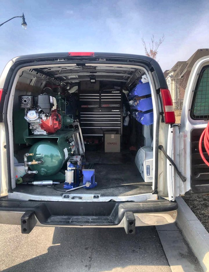 The rear of the Elite Autos Repair service van open, showing a petrol-driven air compressor, a Husky tool chest, a bottle jack and parts bins